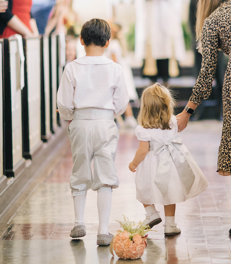 Cute flower girl and older page boy walking down the aisle wearing little eglantine outfits